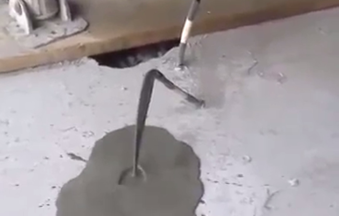 A close-up shot showing liquid grout exiting from a vent at the far end of a duct, confirming the full encasement of tendons in a bonded post tension slab.